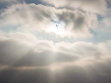 Wispy showing sun partially obscured by wispy clouds with visible sun rays and a soft, diffused light creating a gentle atmosphere. resolutionの素材
