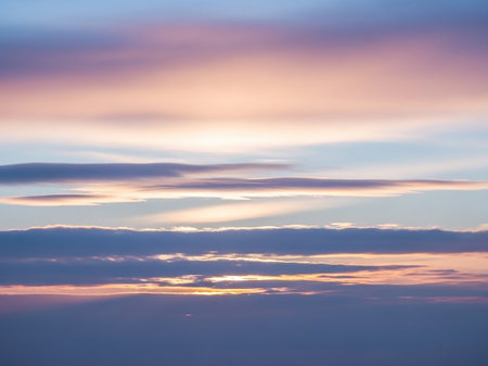 Soft layers of purple and pale orange clouds fill the sky during twilight, with subtle sun rays filtering through the atmospheric haze.の素材