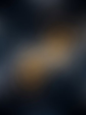 Outoffocus showing softly blurred abstract background with a diagonal band of warm golden light contrasting against dark blue and grey tones keywords: abstract,...の素材