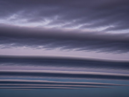 Meteorological showing striking horizontal lenticular clouds layered in a gradient of deep purple and soft lavender hues against a clear blue sky at dusk keywords:...の素材