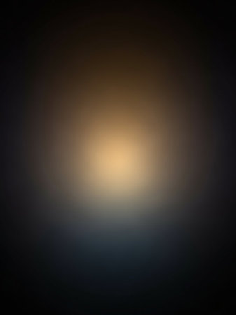 A softly blurred abstract background a bright golden yellow light source at the center, fading into dark grey and black edges.の素材