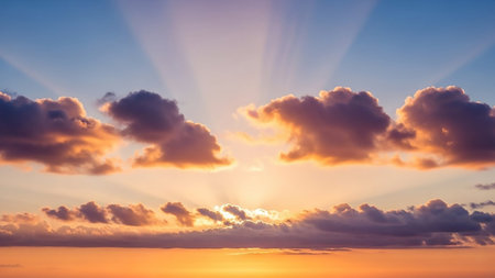 Sunbeams radiate from behind clouds during a vibrant sunrise, creating a dramatic sky with orange, blue, and yellow tones.の素材