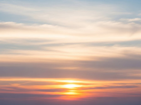 A vibrant sunset a fiery orange sun peeking through soft, hazy clouds with a distinct horizon line in a vertical composition.の素材