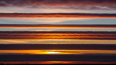 Fiery showing vibrant sunset sky with horizontal layers of fiery orange and red clouds contrasting with deep blue and purple hues creating a striking natural...の素材