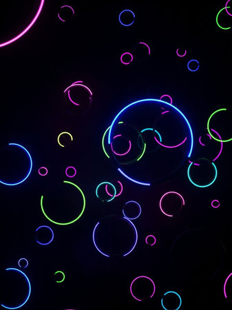 A dark background is filled with scattered neon ring segments and full circles in blue, pink, and green, creating a dynamic, abstract composition.の素材