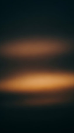 A dark, moody abstract background with two blurred horizontal bands of warm orange light set against a deep navy blue backdrop.の素材