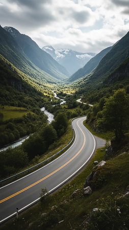 (9398) showing winding asphalt road through a lush green mountain valley with a river and dramatic cloudy sky. resolution use.の素材