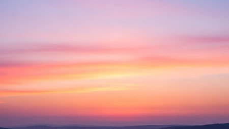 Under showing soft pastel sunset sky with horizontal streaks of pink orange and yellow clouds over a silhouetted mountain horizon under a light purple haze.の素材