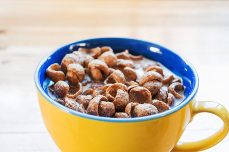 close-up a cup of fresh milk mixed with cereal and red spoon, prepare for breakfast, on wooden table