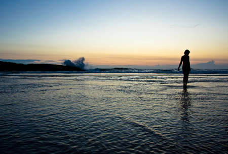 silhouette of a girl on a beach enjoying sunset and strong wavesの写真素材