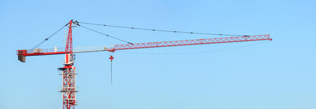 Red and white building tower crane against a blue sky. Jib craneの写真素材