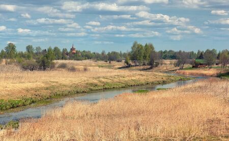Rural landscape with high dry grass on a background of a bend of the river, trees and an abandoned templeの写真素材