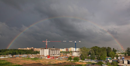 Stormy sky with a full rainbow over the construction site of a residential building with tower cranesの写真素材