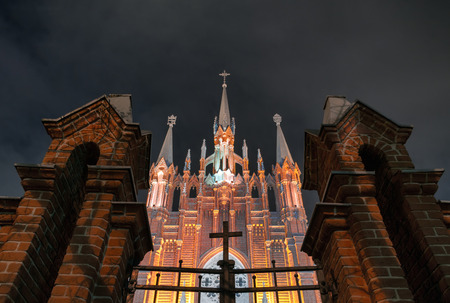 Catholic cathedral in the Gothic style between the brick pillars of the fence with a cross. Night Scene. Focus on the templeの写真素材