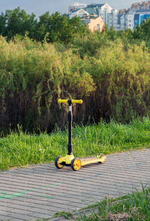 Three Wheel Adjustable Height yellow Scooter on the path of paving tiles in a city parkの写真素材