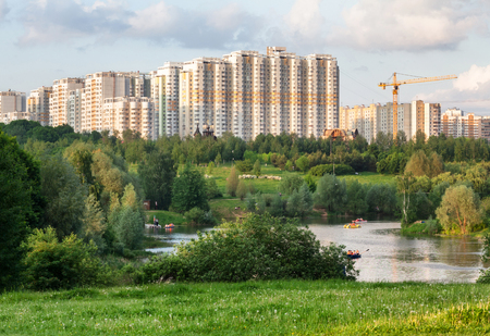 City park with a pond and resting people against the backdrop of modern multistory buildingの写真素材