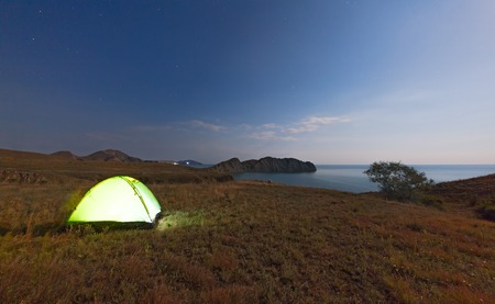Tourist tent on a promontory near the sea on the background of the night sky. The concept of traveling with tentsの写真素材