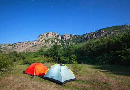 Tourist tents in a clearing in the mountains against the starry sky and the mountain peakの写真素材