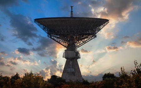 Silhouette of an old huge radio telescope to ensure the launch of spacecraft to the moon against the backdrop of the rays of the setting sunの写真素材