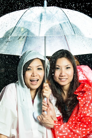 Asian women under the rain with rain coat and umbrellaの写真素材