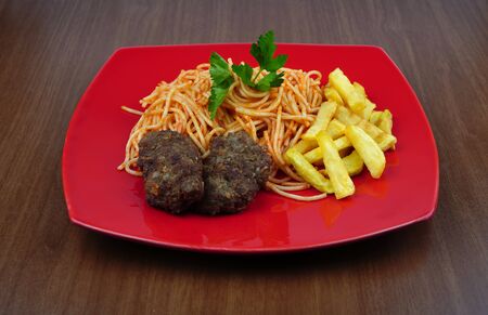 Pasta, meatballs and potatoes on a red plate on the tableの写真素材