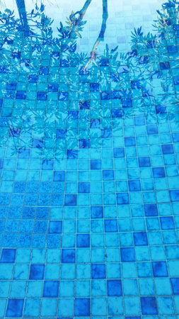 A serene swimming pool framed by chairs and lush trees, offering an idyllic escape for relaxation and leisureの写真素材