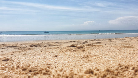 A tranquil beach on Bali's Nusa Penida island, marked with solitary footprints in the sand and a distant boat, capturing the essence of serene seclusionの写真素材