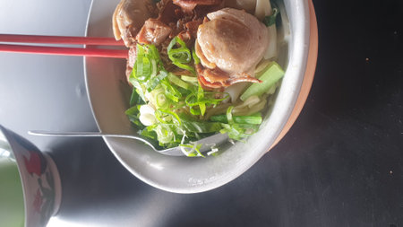 A mouthwatering bowl of Asian culinary delight featuring savory leeks and succulent meatballs, accompanied by chopsticks, resting on a well-set tableの写真素材
