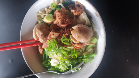 A mouthwatering bowl of Asian culinary delight featuring savory leeks and succulent meatballs, accompanied by chopsticks, resting on a well-set tableの写真素材