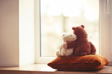 Two embracing teddy bears looking through the window sitting on window-sill の写真素材