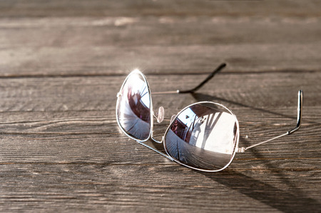 Metal thin trendy sunglasses on wooden table. Evening light.  Outdoors closeup.の写真素材