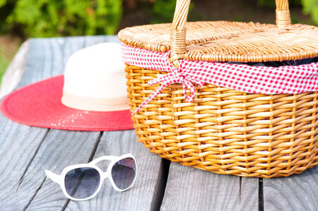 Ready for summer weekend. White sunglasses summer hat and wicker basket on wooden table outdoors.の写真素材