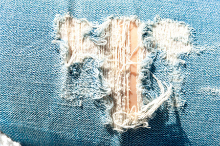 Torn frayed hole in blue denim texture. Outdoors closeup.の写真素材