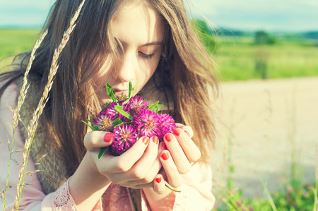 Beauty of nature  Young beautiful girl smelling meadow clover flowers outdoors  Vintage retro filter の写真素材