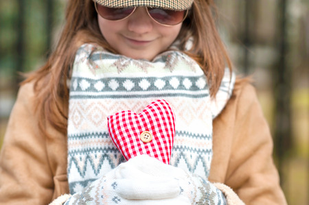 Smiling girl in white knitted mittens holding romantic red heart. With Love. Valentineの写真素材