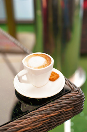 White porcelain cup of black coffee with whipped milk on rattan table in summer cafe. Outdoors closeup.の写真素材