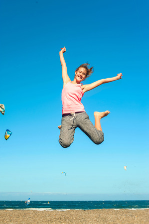 I Believe i can fly! Excitement of young cheerful jumping teenage girl on the windy beach of Atlantic ocean. Canary islands, Tenerife, Spain. Vibrant summertime outdoors vertical image.の写真素材