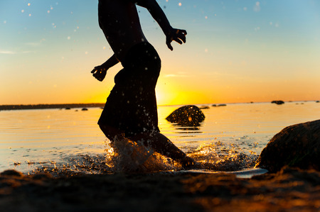 Summertime fun on the beach for joy. Running man silhouette on sunset background. Multicolored vibrant outdoors horizontal image.の写真素材