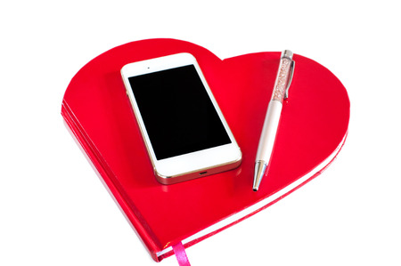 Smartphone pen and red heart shaped notebook on white background. Indoors horizontal image.の写真素材