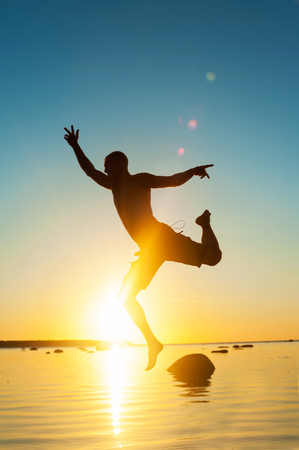 Funny jumping on the beach for joy. Funny jumping man silhouette on spectacular sunset background. Multicolored vibrant vertical outdoors image.の写真素材
