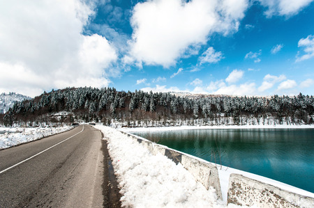 Frozen lake and road to snowy woodland in winter Georgia. Shaori lake, Racha. Caucasus. Colorful vibrant outdoors horizontal image with perspective.の写真素材