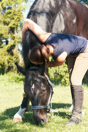 Young girl equestrian saddling horse eating grass. Colored outdoor vertical image.の写真素材