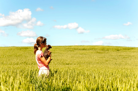 Young teenage girl in wheat field holding her lovely little toy-terrier dog contemplating the nature. Multicolored vibrant outdoors summertime horizontal image with cloudy sky background.の写真素材