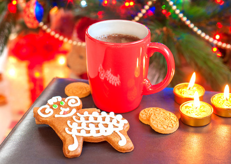 Sheep shape gingerbread cookie with cup of coffee on illuminated christmas tree background. Festive...