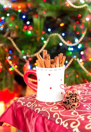 Cup with cinnamon sticks on festive christmas tree background. Celebration indoors still-life.の写真素材