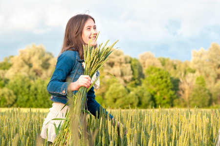 Happy cheerful young girl walking and picking stems on wheat field. Summertime outdoors.の写真素材