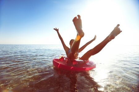Silhouette of funny young teenage girl having fun on inflatable ring in Mediterranean sea with arms and legs rised up. Summertime outdoors inspirational horizontal image with vintage filter.の写真素材