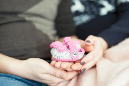 Young happy future parents hands holding woollen knitted newborn baby booties. Indoors horizontal colored close-up image with soft vintage filter.の写真素材