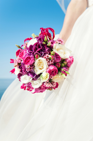 Bride hand holding flower bouquet on blue sky background. Vibrant colored summertime outdoors close-up vertical image with filter. Low point of view.の写真素材