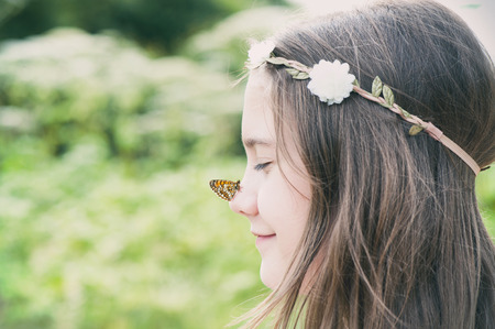 Portrait of boho style cheerful girl with floral headband on head and butterfly on nose. Summertime horizontal  outdoors image with vintage filter.の写真素材